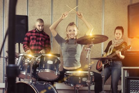 Music garage band with expressive glad girl drummer rehearsing in sound studio