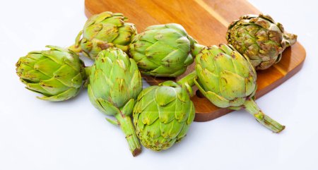 Pile of fresh ripe artichokes on wooden cutting board on white background. Organic vegetarian food concept..