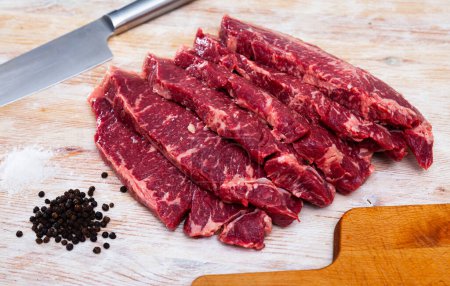 Fresh raw beef meat with pepper spices and knife on light wooden background