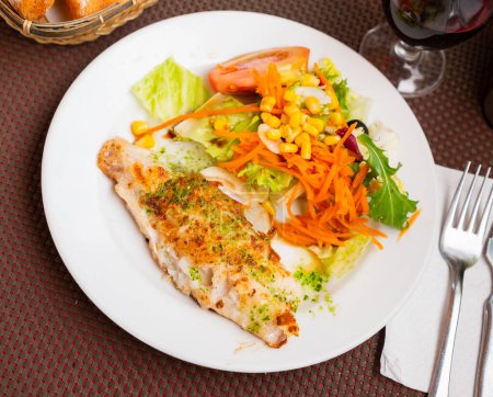 Appetitlich frittiertes Fischfilet, gehackte Petersilie und Knoblauch in Olivenöl serviert mit frischem Gemüsesalat auf Teller.
