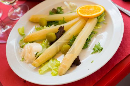 Delicious white asparagus sous vide garnished with hollandaise sauce, greens and orange