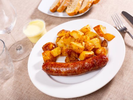 Appetizing fried meat sausages with potatoes and alioli sauce served on platter..