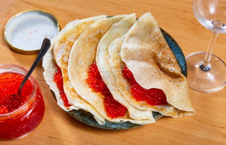 Thin crepes served in a plate with red caviar and other table appointments