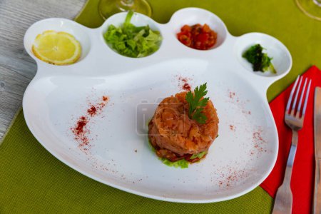 Tasty tartar from salmon served with vegetables and lemon on white plate..