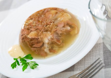 Traditional russian dish kholodets served on table with chrain and parsley sprig.
