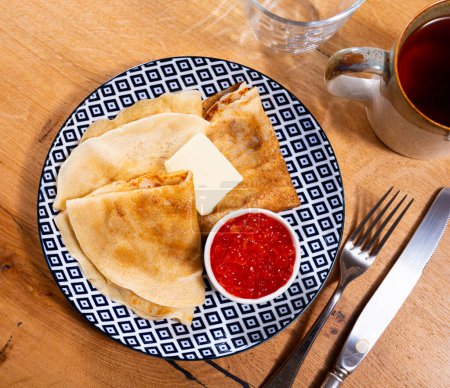 Los panqueques recién hechos se complementan con mantequilla y porción de caviar rojo. El plato es un manjar casero para el desayuno familiar..