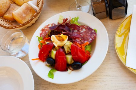 Köstlicher Salat mit frischem Salat, Tomaten, geriebener Karotte und Ei bedeckt mit dünnen Scheiben verschiedener Würstchen. Katalanische Küche..