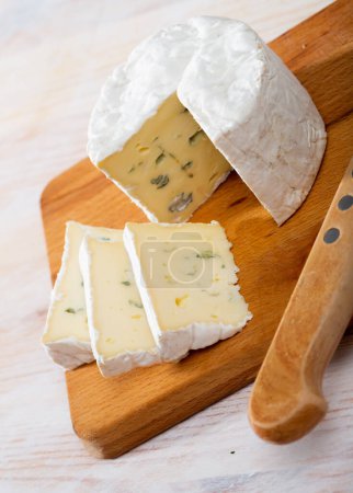 Wheel of delicate blue cheese with cut slices on wooden cutting board..