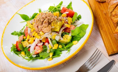 Delicious salad with fresh tomatoes, avocado, canned tuna, onion, corn and greens