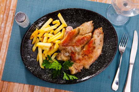Plat de viande avec cuisses de porc cuites au four et frites décorées de feuilles de persil