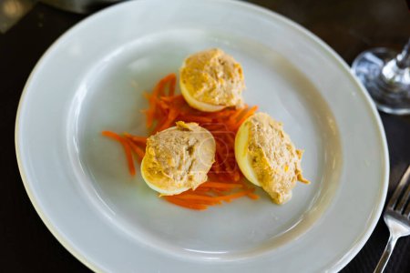 Several boiled chicken eggs with meat filling are laid out on plate. Snack is on top of salad of grated fresh carrots.