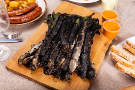 Traditionelle Gerichte Kataloniens, Calcot mit Rommesco-Sauce auf Holzbrett, Brot und gegrillte Butifarra-Wurst auf dem Tisch