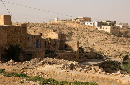 Logements en pierre usés par le soleil de Tamezret, ancien village berbère à flanc de colline dans le gouvernorat de Gabes, se mélangeant avec un paysage tunisien aride