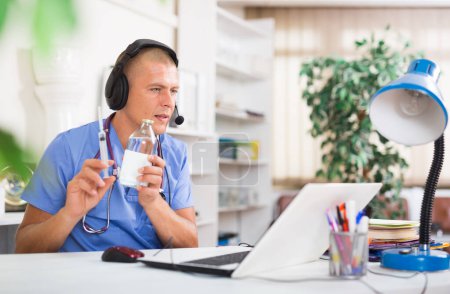 Médecin qualifié dans les écouteurs ayant une consultation en ligne avec le patient sur ordinateur portable dans le bureau de la clinique..
