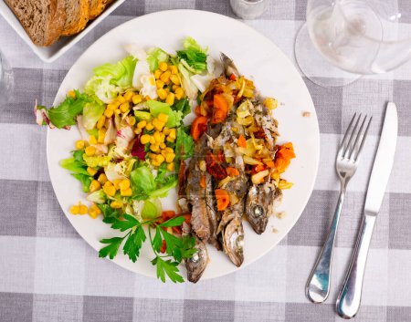 Roasted poutassou with lightly fried carrot and onion and vegetable salad with corn, popular spanish dish