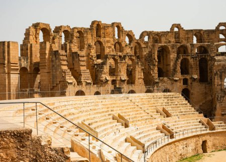 Interior of El Jem Amphitheatre with tiers of restored stone seating rising around central arena and surrounded by remnants of walls with arched passageways. Grandeur of Roman architecture in Tunisia