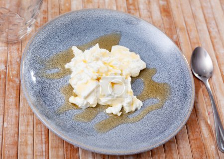 Typical dish of Catalan cuisine - delicate homemade fresh whey cheese mato from goat milk dressed with honey on plate. Popular dairy product