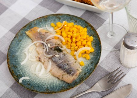 Délicieux hareng de mer tranché servi avec du maïs et des oignons sur une assiette ronde avec fourchette au restaurant