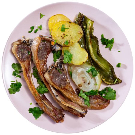 There are fried lamb ribs on plate. Meat appetizer is complemented with baked potatoes, bell peppers, onion and sprinkled with chopped herbs. Isolated over white background