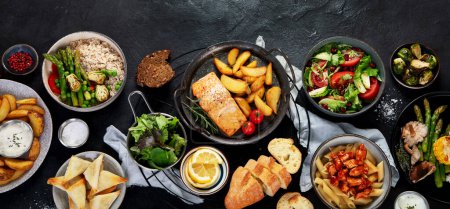 Set of various main dishes. Different healthy main courses, meat and fish dishes, pasta, salads, sauces, bread and vegetables on a dark background. Top view, panorama