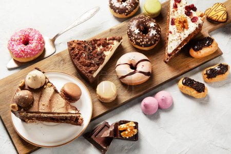 Photo for Selection of various cake pieces, macaroons, meringues, cookies and donuts on a wooden desk on a light background. Top view. Confectionery background. - Royalty Free Image