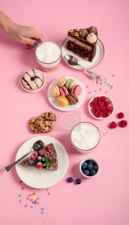 Foto de Mesa con varias galletas, rosquillas, pasteles, tartas de queso y tazas de café sobre fondo rosa. Deliciosa mesa de postres. Vista superior - Imagen libre de derechos