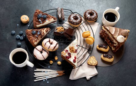 Foto de Mesa con varias galletas, rosquillas, pasteles, tartas de queso sobre fondo oscuro. Deliciosa mesa de postres. Vista superior, plano - Imagen libre de derechos