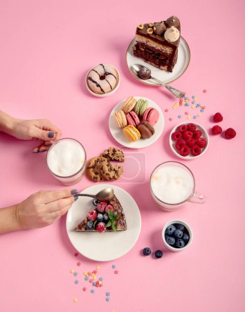 Foto de Mesa con varias galletas, rosquillas, pasteles, tartas de queso y tazas de café sobre fondo rosa. Deliciosa mesa de postres. Vista superior, plano - Imagen libre de derechos