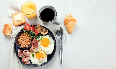 Téléchargez les photos : Petit déjeuner anglais complet avec œufs frits, saucisse, bacon et pain grillé sur fond gris. Vue du dessus, espace de copie - en image libre de droit