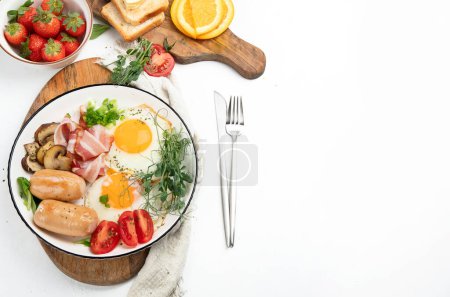 Englisches Frühstück mit Spiegelei, Wurst, Speck und Toast auf weißem Hintergrund, Draufsicht, Kopierschutz