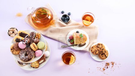 Foto de Té tradicional inglés. Té de la tarde con selección de dulces sobre fondo violeta. Concepto de vacaciones - Imagen libre de derechos