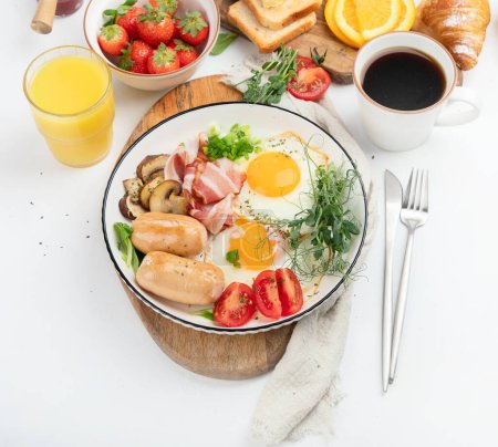 Téléchargez les photos : Petit déjeuner anglais avec œuf frit, saucisse, bacon et pain grillé sur fond blanc - en image libre de droit