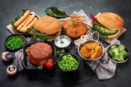 Foto de Hamburguesas vegetarianas, salchichas, nuggets vegetarianos, verduras frescas y salsas en un fondo oscuro. vista superior. - Imagen libre de derechos