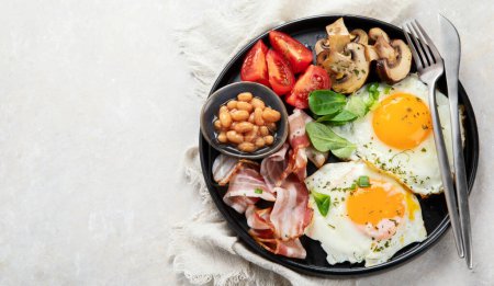 Foto de Desayuno inglés completo con huevo frito, salchichas, tocino y tostadas sobre fondo gris. Vista superior, espacio de copia - Imagen libre de derechos
