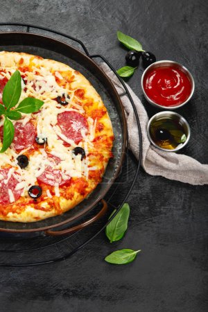 Foto de Freshly baked pepperoni pizza on dark background. Tasty homemade food concept. Top view, copy space - Imagen libre de derechos