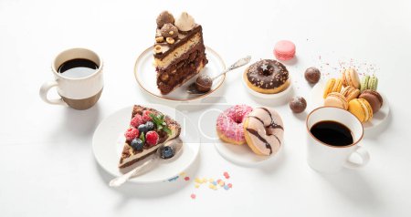 Foto de Mesa con varias galletas, rosquillas, pasteles, tartas de queso y tazas de café sobre fondo blanco. Deliciosa mesa de postres. - Imagen libre de derechos