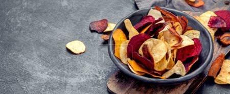 Foto de Cuenco de chips vegetales coloridos saludables sobre fondo oscuro, espacio de copia - Imagen libre de derechos
