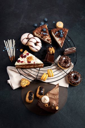 Foto de Mesa con varias galletas, rosquillas, pasteles, tartas de queso sobre fondo oscuro. Deliciosa mesa de postres. Vista superior, plano - Imagen libre de derechos