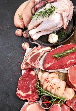 Téléchargez les photos : Différents types de viande crue - bœuf, porc, agneau, poulet sur fond sombre. Vue du dessus, espace de copie - en image libre de droit