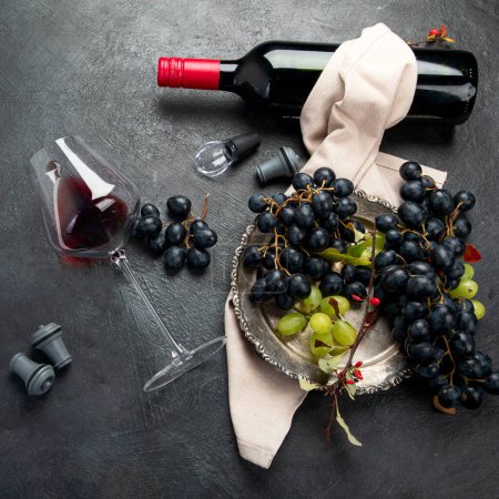 Photo for An overhead photo of glasses of red wine with a bottle, grapes, and a vintage corkscew and corks, shot from above on a dark background. Top view. - Royalty Free Image