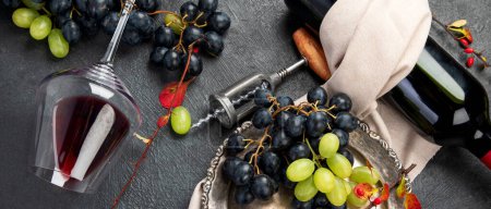 Photo for An overhead photo of glasses of red wine with a bottle, grapes, and a vintage corkscew and corks, shot from above on a dark background. Top view. Panorama. - Royalty Free Image