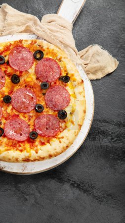 Foto de Freshly baked pepperoni pizza on dark background. Tasty homemade food concept. Top view, copy space - Imagen libre de derechos