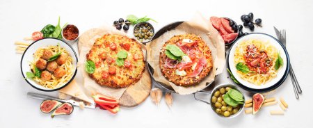 Photo for Full table of italian meals on plates  and board - Pizza, pasta, meatballs, salami, parmesan, olives, bread sticks on a white background. Top view. Panorama. - Royalty Free Image