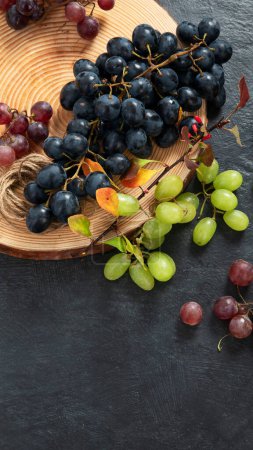 Téléchargez les photos : Raisins verts et noirs sur une assiette en bois. Vue du dessus. - en image libre de droit