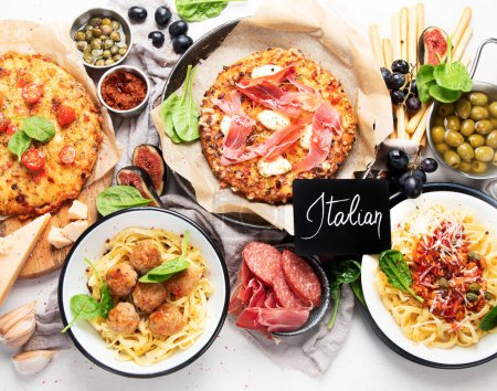 Photo for Full table of italian meals on plates  and board - Pizza, pasta, meatballs, salami, parmesan, olives, bread sticks on a white background. Top view. - Royalty Free Image