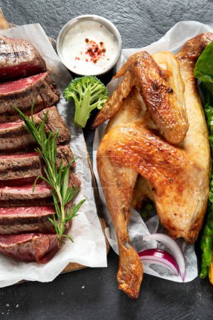 Téléchargez les photos : Différents types de viande cuite saine - bœuf, porc, poulet sur fond sombre avec légumes et salade. Vue du dessus. - en image libre de droit
