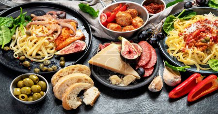 Téléchargez les photos : Dinner table of italian meals dishes.  Pizza, pasta, antipasto  on black background. Healthy eating concept. - en image libre de droit