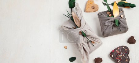 Téléchargez les photos : Zero waste Valentine's Day concept. Eco-friendly gift cloth wrapping in Furoshiki style, homemade sweets and cookies as gift ideas on white background. Top view or flat lay. Panorama with copy space. - en image libre de droit