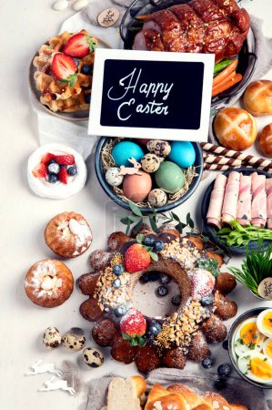 Téléchargez les photos : Traditional Easter dinner or  brunch with ham, colored eggs, hot cross buns, cake and vegetables. Easter meal dishes with holday decorations. Top view - en image libre de droit