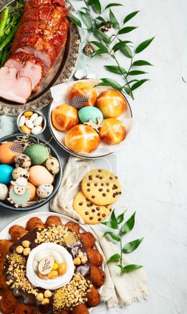 Téléchargez les photos : Classic Easter ham dinner. Top view table scene on a white background. Ham, eggs, hot cross buns, carrot, cake and vegetables. - en image libre de droit